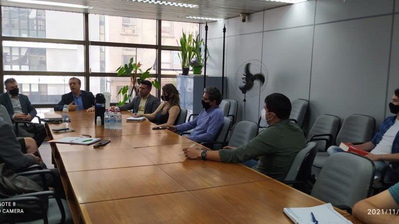 Reunião com homens e mulheres ao redor de uma mesa.