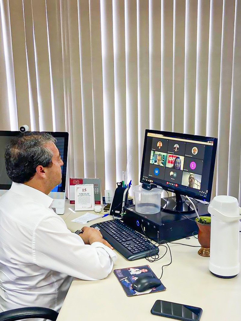 Secretário Ronaldo está sentado, vestindo uma camisa branca, em reunião online. Na mesa tem uma chimarrão e uma térmica