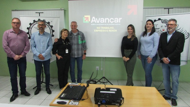 Sete pessoas posando para a foto, atrás está a tela com o programa avançar no trabalho, emprego e renda. São três mulheres e quatro homens