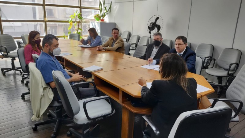 reuniao do conselho - em uma mesa de reuniões, três mulheres e quatro homens participam do reunião do CETER. Ao fundo temos uma janela, folhagens e um ventilador