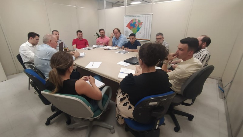 Equipe reunida na sala de reunião com materiais de trabalho em cima da mesa.