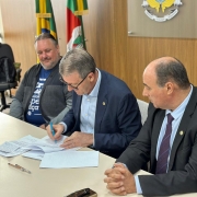 Secretário Gilmar Sossella assinando o termo de colaboração. O presidente da Avesol, Miguel Orlandi, e o deputado estadual Zé Nunes, estão sentados ao lado dele. 