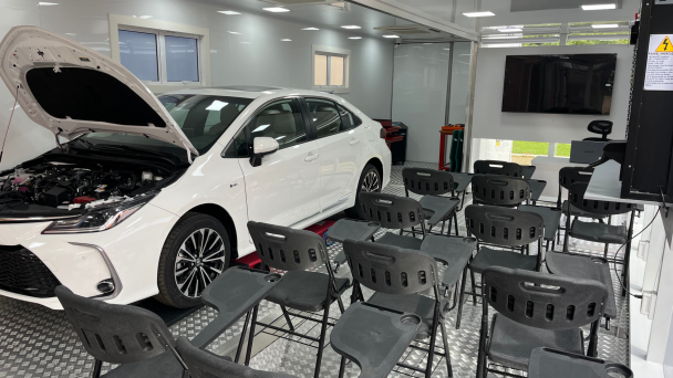 Imagem tem cadeiras vazias e um carro com o cap&ocirc; aberto em uma sala de aula dentro de uma unidade m&oacute;vel do programa Carretas do Saber