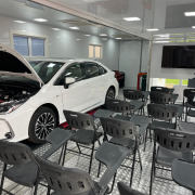 Imagem tem cadeiras vazias e um carro com o cap&ocirc; aberto em uma sala de aula dentro de uma unidade m&oacute;vel do programa Carretas do Saber